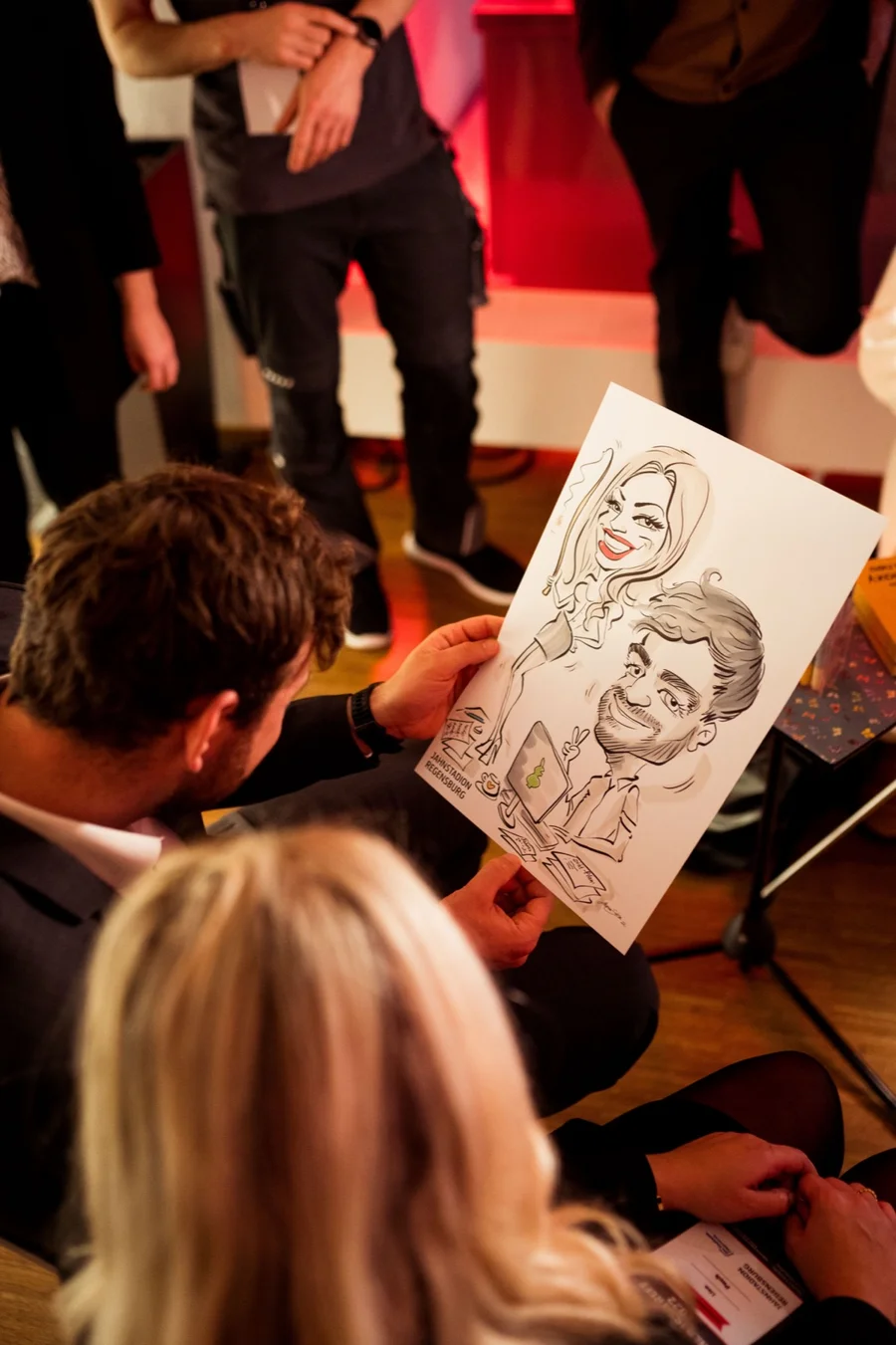 Karikaturist zeigt Gästen einer Veranstaltung seine Zeichnung