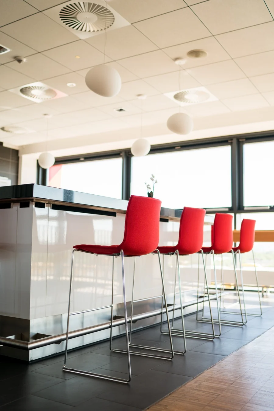 Stehtische mit roten Barhockern vor Panoramafenstern in der Business-Lounge