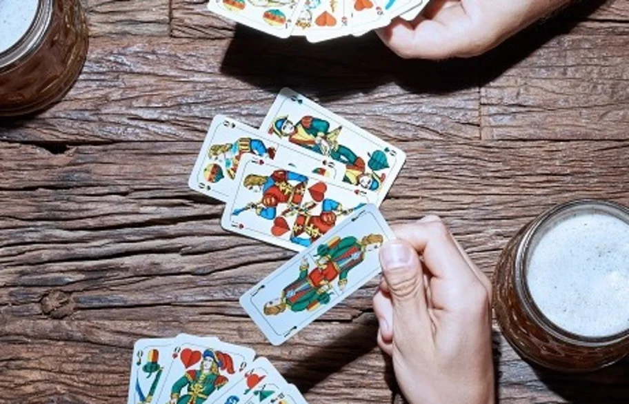 Hände mit bayerischen Spielkarten und Bierkrügen beim Schafkopf