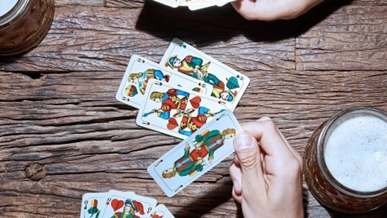 Hände mit bayerischen Spielkarten und Bierkrügen beim Schafkopf