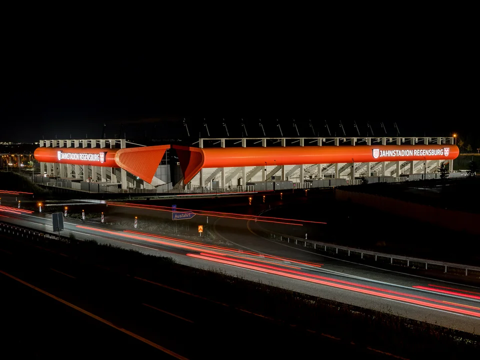 Beleuchtetes Jahnstadion bei Nacht mit Lichtspuren auf der A3