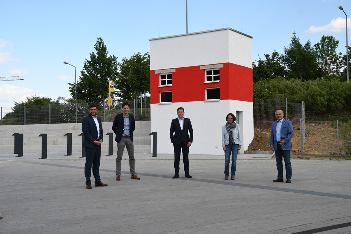 Man sieht fünf Personen die mit Abstand vor einem Rot-Weißen Turm stehen.
