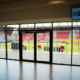 Besondere Ausblicke. Man sieht den Blick in den Innenbereich mit Rasen und Tribüne des Jahnstadions durch eine große bodentiefe Fensterfront.
