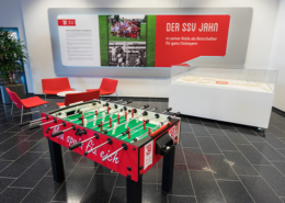 Man sieht einen Kicker im SSV Jahn Regensburg Design sowie eine Deko an der Wand über den SSV Jahn.