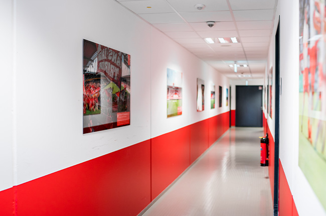 Man sieht einen Gang im Jahnstadion. An der Wand hängen Bilder und die Wand ist bis zur Hälfte rot gestrichen.