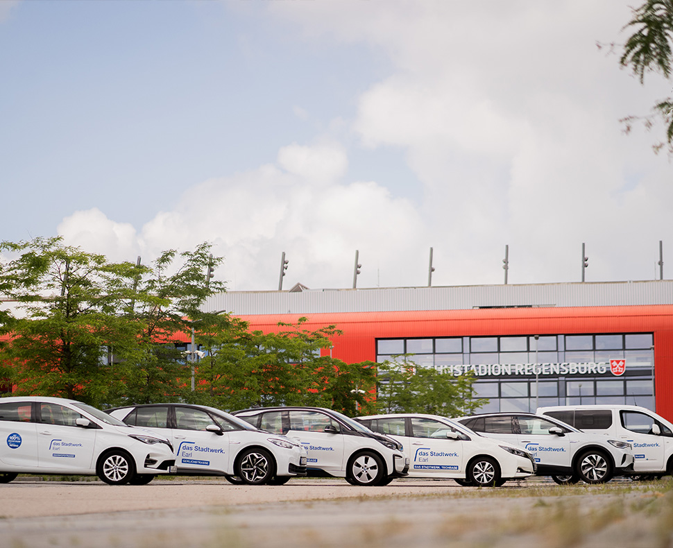 Man sieht sechs weiße Autos verschiedener Marken, die vor dem Jahnstadion in einer schrägen Reihe nebeneinander parken.