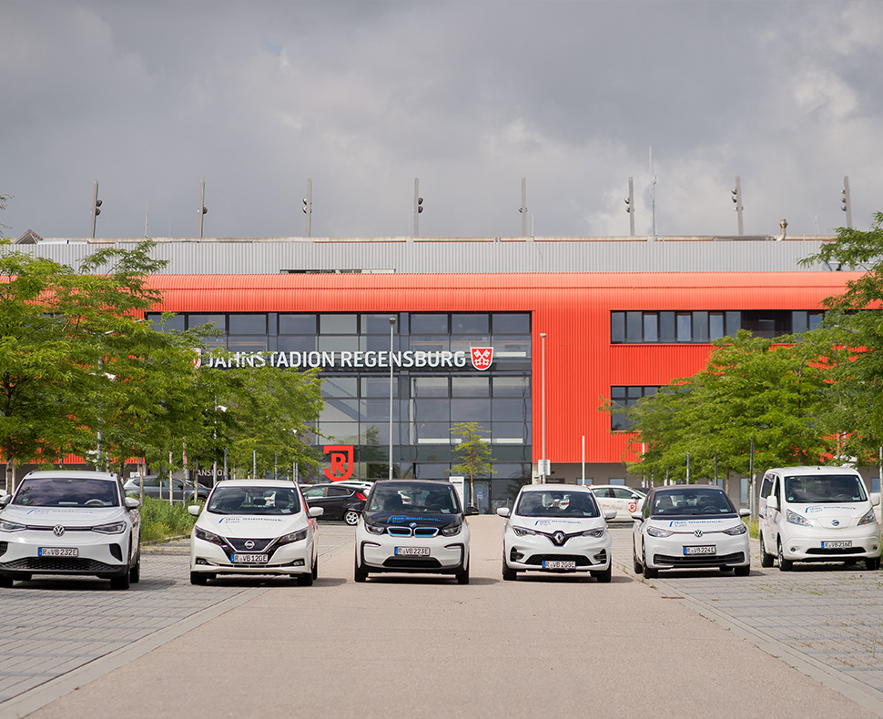 Man sieht sechs weiße Autos verschiedener Marken, die vor dem Jahnstadion in einer geraden Reihe nebeneinander parken.