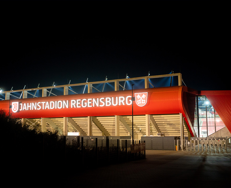 Man sieht die Rückseite einer Tribüne mit dem Schriftzug Jahnstadion Regensburg bei Nacht.