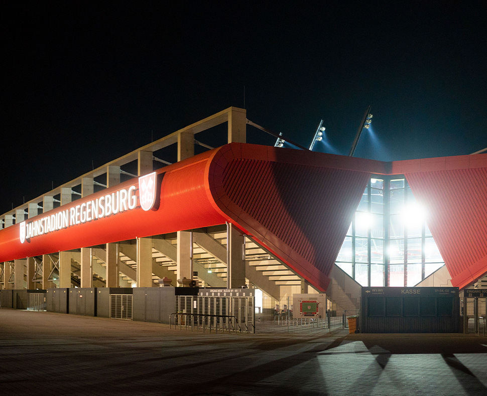 Man sieht ein Foto vom Jahnstadion Regensburg bei Nacht mit leuchtender Flutlichtanlage.