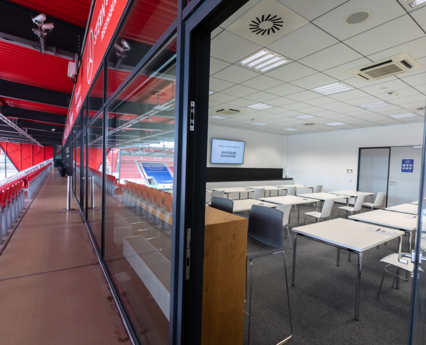 Man sieht den Blick vom Balkon im Jahnstadion, auf der einen Seite in einen Tagungsraum mit Plenarbestuhlung und auf der anderen Seite auf die Tribüne mit roten Stühlen.