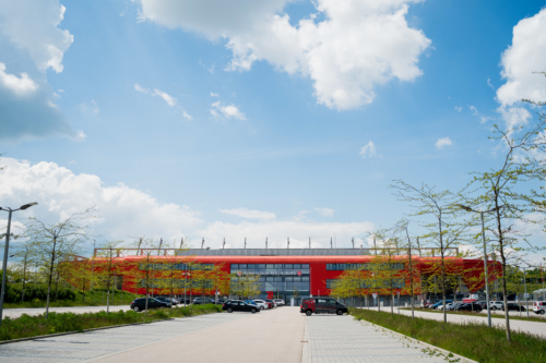 Man schaut über eine Straße auf die Längsseite des Jahnstadions. Im Hintergrund ist blau-weißer Himmel.