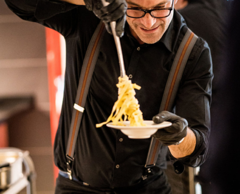Man sieht einen Mann, der Nudeln auf einen Teller portioniert.
