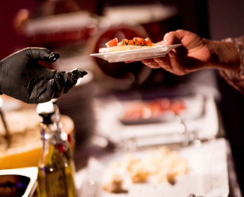 Man sieht eine Hand, die einer anderen Hand an einem Buffet einen Teller übergibt.