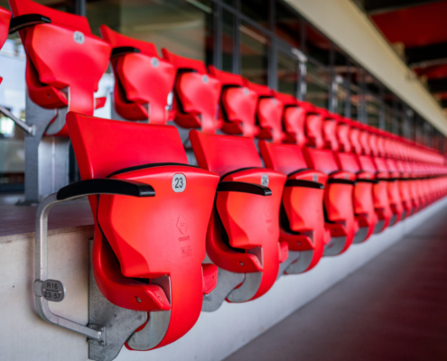Man sieht eine Nahaufnahme von roten Klappstühlen in einem Sportstadion.