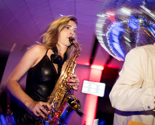 Man sieht eine Frau, die Saxophon spielt. Im Hintergrund sieht man eine Diskokugel.