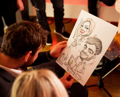 Man sieht zwei Personen, die eine Karikatur in der Hand halten, die zwei Personen zeigt.
