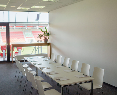 Man sieht einen langen weißen Tisch mit 12 weißen Stühlen in einem Tagungsraum des Jahnstadion.