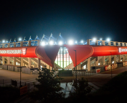 Man sieht ein Foto vom Jahnstadion Regensburg bei Nacht mit leuchtender Flutlichtanlage.