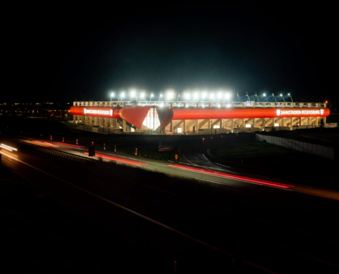 Man sieht ein Foto vom Jahnstadion Regensburg bei Nacht mit leuchtender Flutlichtanlage von weiter weg.