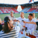 Man sieht eine Gruppe Menschen, die an einem Tisch anstoßen, der im Jahnstadion steht.