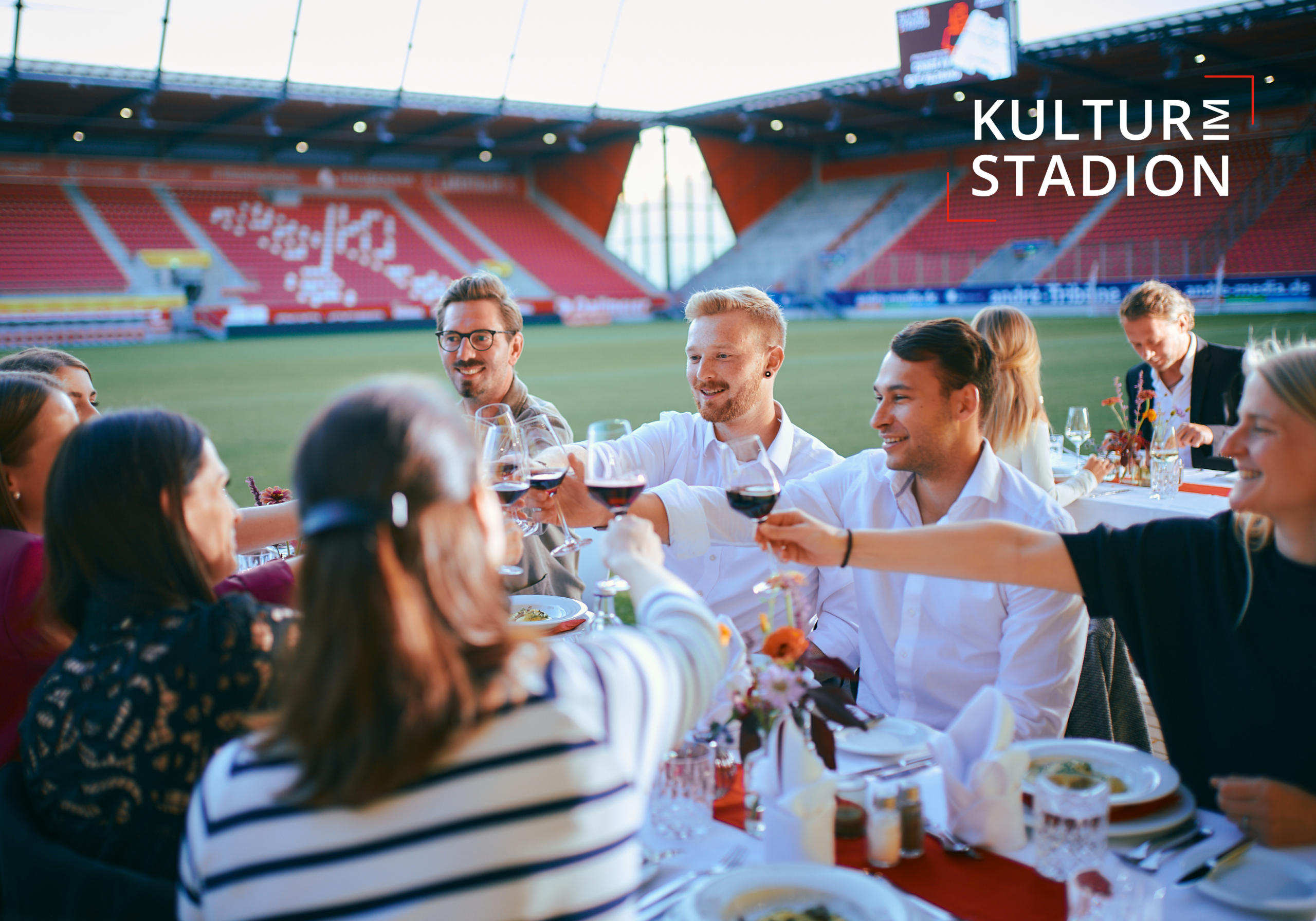 Man sieht eine Gruppe Menschen, die an einem Tisch anstoßen, der im Jahnstadion steht.