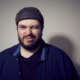 Man sieht das Gesicht eines Mannes mit Mütze, der in die Kamera zwinkert.