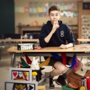 Man sieht ein Foto von einem Jungen mit Zauber-Ausrüstung in einen Klassenraum sitzen.