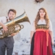 Man sieht ein Foto von Franziska Wanninger und Martin Frank, in dem beide in Tracht angzogen sind und Martin Tuba spielt.