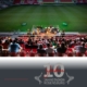 Man sieht eine Bühne mit Musikern, die vor mehrere Menschen auf der Tribüne spielen, im Hintergrund sieht man den Rasenplatz des Jahnstadions und darunter sieht man das 10 Jahre Jubiläumslogo.